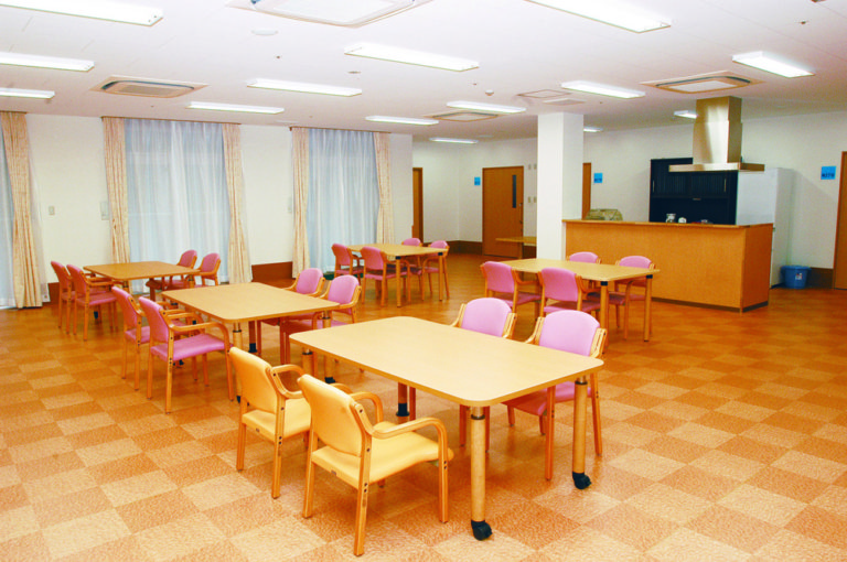 介護施設の広々としたダイニングスペース。複数のテーブルと椅子が配置されており、明るく清潔な空間。